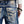 Load image into Gallery viewer, Close-up of blue jeans with intricate designs and branding on a white background
